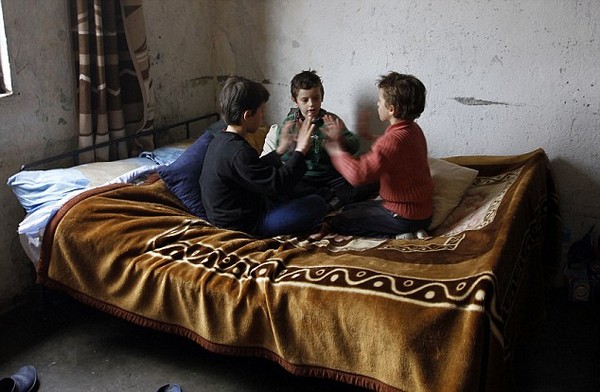 Three children, who have spent their entire childhood locked inside their home, play on their bed in Bardhaj