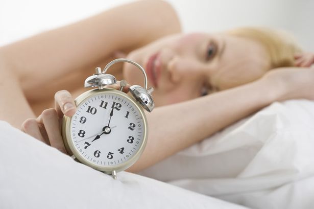 A woman in bed holding an alarm clock-773258