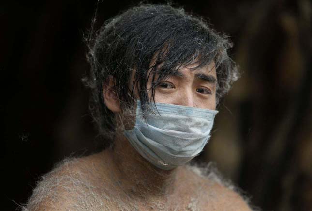 A worker is covered by pieces of fur as he trims raccoon dog fur outside a store at a fur market in Chongfu township