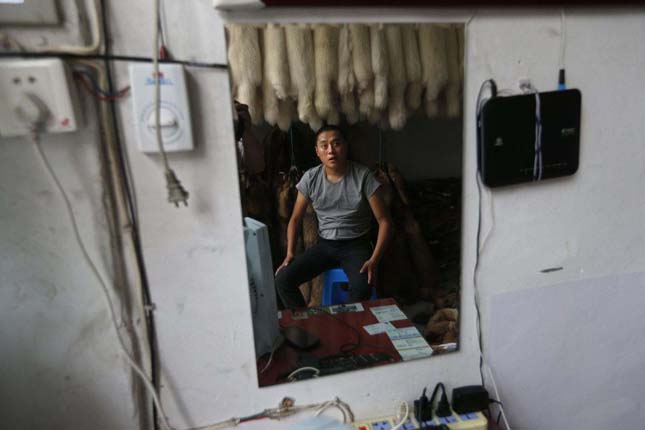 A vendor is reflected in a mirror as he sits under bundles of rabbit fur inside a store at a fur market in Chongfu township