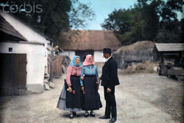 Two women and a man visit in a village wearing folk costume