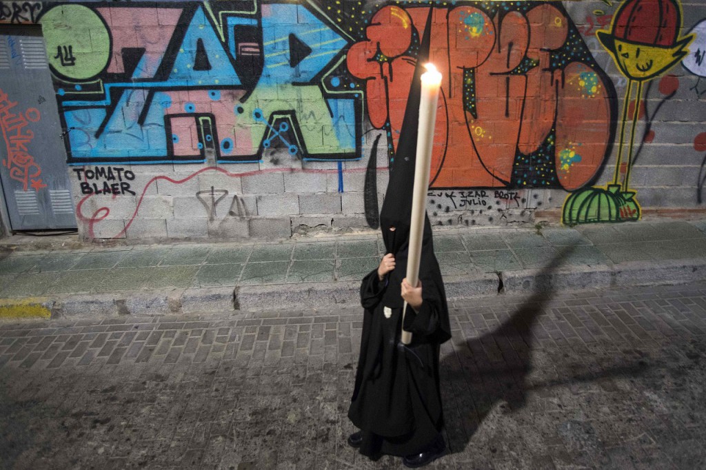Penitent of the Brotherhood of La Soledad holds a candle as he walks past graffiti while taking part in a Holy Week procession in Almeria