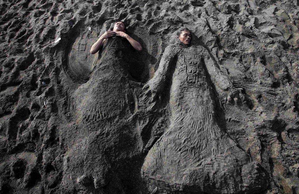 Two men are covered in sand at a beach to celebrate Easter Sunday in Cavite