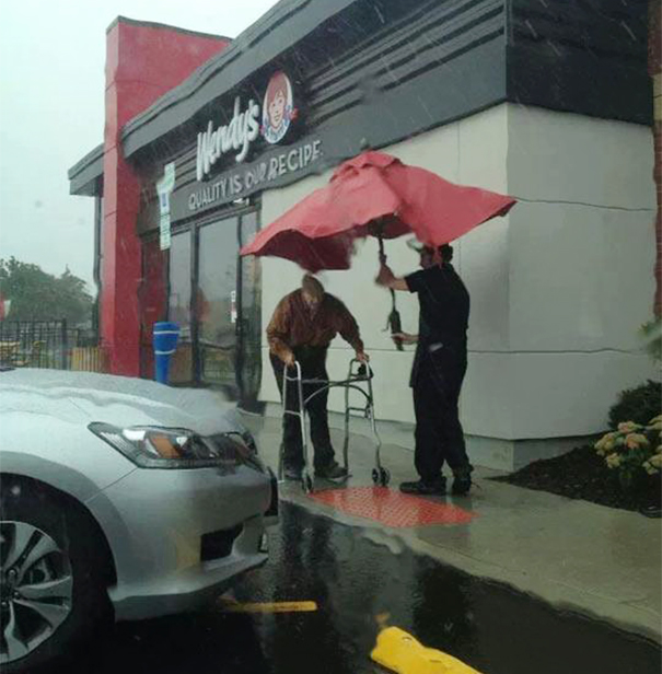 Egy alkalmazott esernyőt adott a mozgáskorlátozott időseknek a gyorsétterem előtt