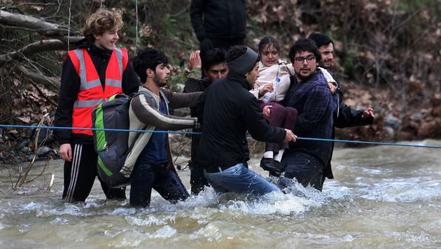 Migrants and refugees cross a river on their way to Macedonia from a makeshift camp at the Greek-Macedonian border near the Greek village of Idomeni where thousands of them are stranded by the Balkan border blockade on March 14, 2016. Hundreds of desperate migrants were stopped by Macedonian troops after wading thigh-deep through a surging river to cross the border from Greece, where thousands have been left stranded after Balkan states slammed Europe's migrant door shut. / AFP PHOTO / SAKIS MITROLIDIS