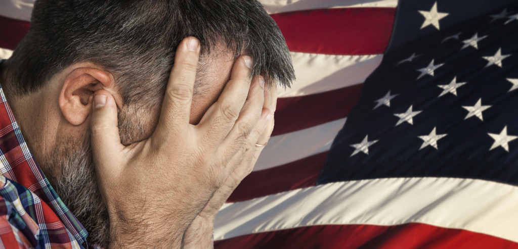 Veteran. Portrait of an elderly man with face closed by hand on USA flag background.
