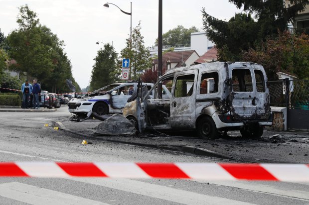 People gather near a burned police vehicle and a van in Viry-Chatillon on October 8, 2016 after police in their patrol car were attacked by individuals who launched Molotov cocktails, leaving two officers injured. Two officers were "seriously injured" when ten individuals launched Molotov cocktails at their vehicle, according to a police source. The officers in their vehicle were responsible for monitoring footage from a camera near a traffic light in Viry-Chatillon. / AFP PHOTO / Thomas SAMSONTHOMAS SAMSON/AFP/Getty Images